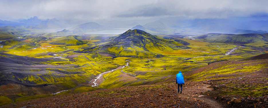 Ein Mann mit blauem Wanderrucksack bewundert die faszinierende Landschaft Islands