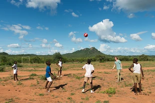 A student of TUM plays soccer on a field of red soil with pupils from Marymount, Zimbabwe