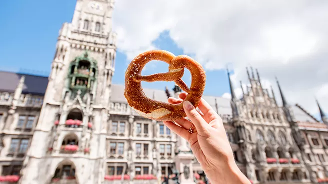 Hand holding a traditional Bavarian pretzel, Munich City Hall in the background