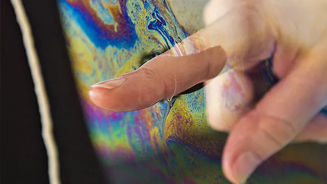 Finger taucht in irisierende Flüssigkeit