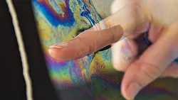 Finger taucht in irisierende Flüssigkeit
