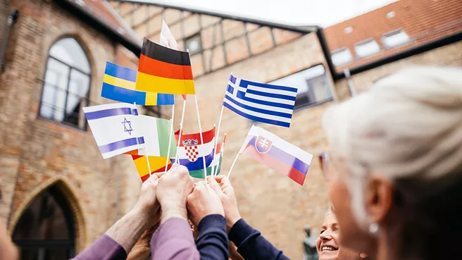 Hochschulvertreter:innen halten Fähnchen mit den Flaggen verschiedener europäischer Länder in die Luft