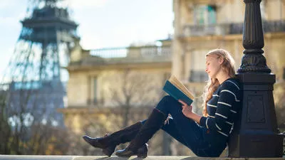 Studentin liest mit Blick auf den Eiffelturm in einem Buch