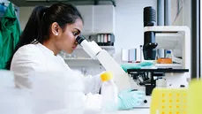 Junge indische Wissenschaftlerin beobachtet durch Mikroskop im Labor