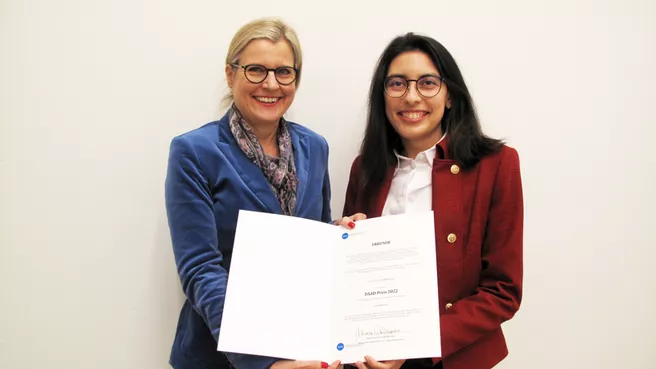 Two smiling women jointly present a certificate to the camera