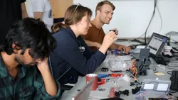Junge Menschen arbeiten mit Laptops und Werkzeugen an einem Schreibtisch