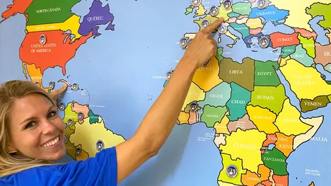 The TUM employee in front of a colorful world map