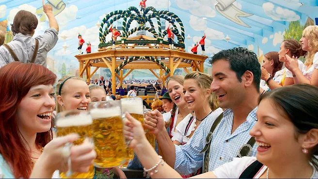 Joyful people wearing Bavarian garb clink their beer mugs in a beer tent