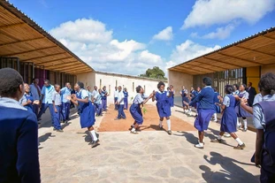Zambian pupils in blue uniforms run happily across their newly built school yard