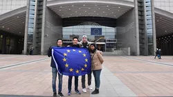 Vier Studierende mit großer Europa-Flagge vor dem EU-Parlament in Brüssel