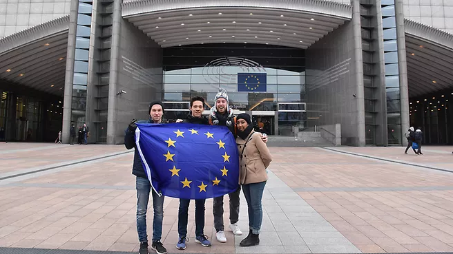Four students with big Europe flag in front of the EU Parliament in Brussels