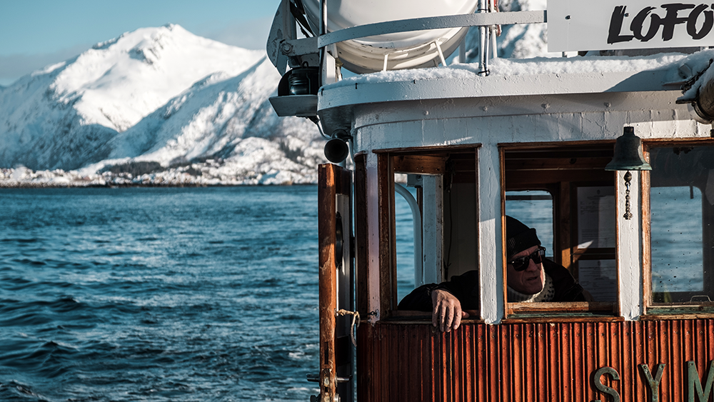 Ein Fischer auf seinem Boot vor der vereisten Kulisse Nordnorwegens