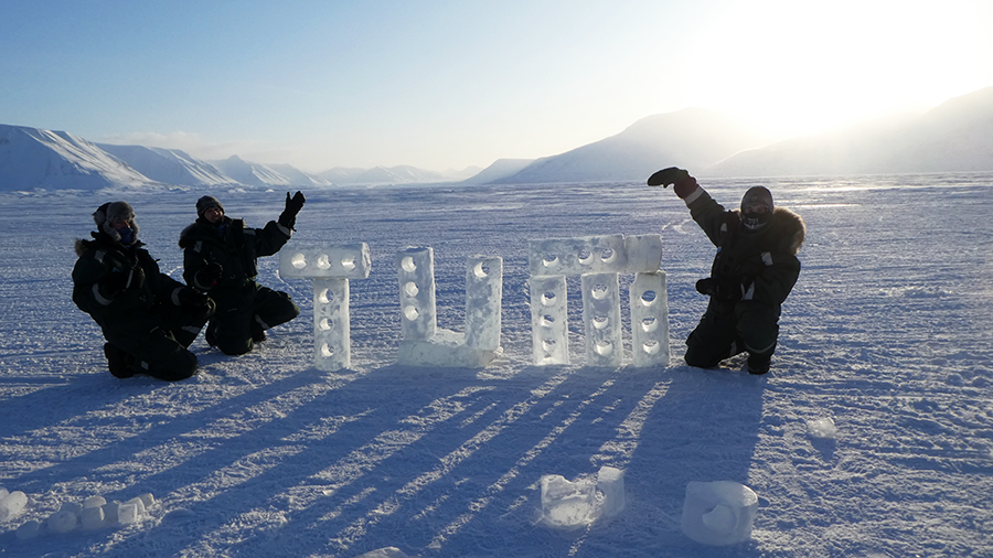 Students of TUM pose next to the ice sculpture of the TUM logo they created