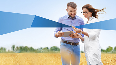 Two people standing in a grain field with a tablet