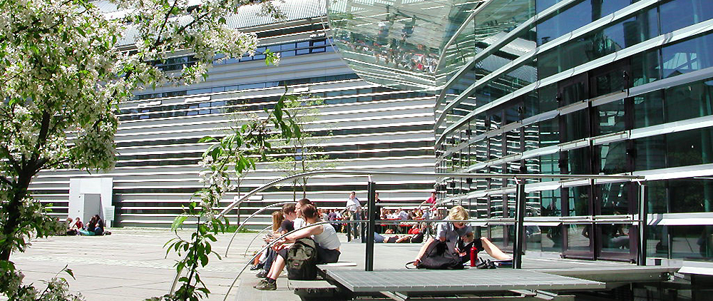 Studierende sitzen vor dem Audimax der TUM in der Sonne