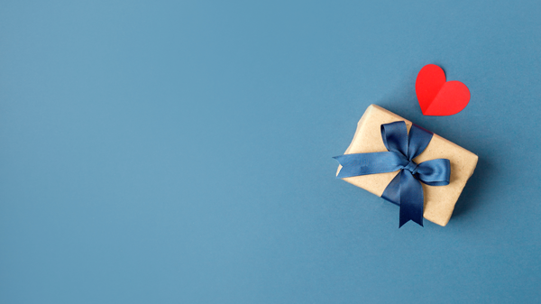 Geschenk-Box mit blauer Schleife und ein rotes Herz auf blauem Hintergrund 