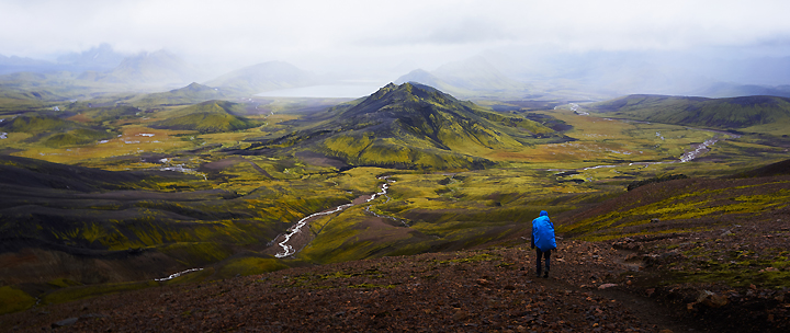 Ein Mann mit blauem Wanderrucksack bewundert die faszinierende Landschaft Islands